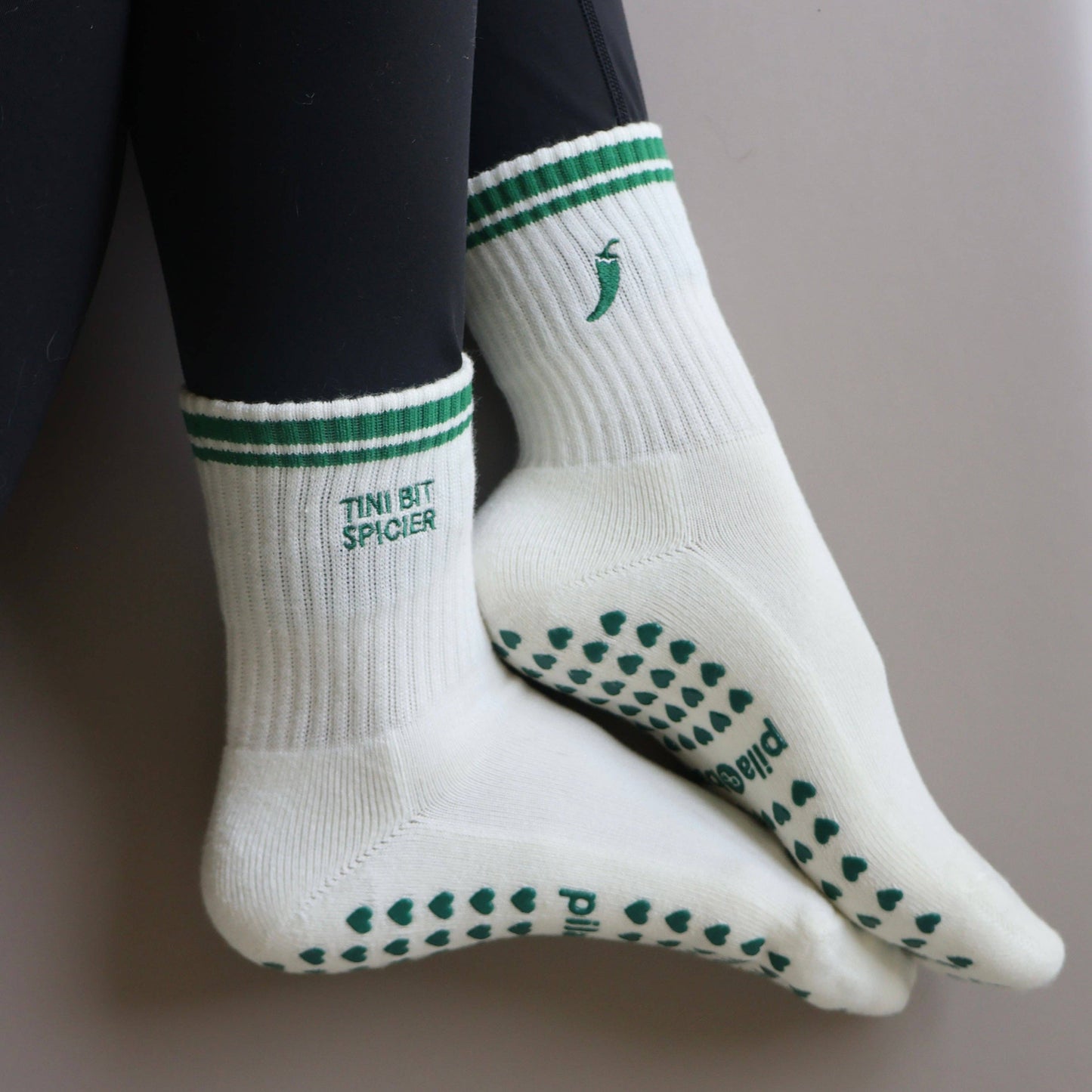 White and green Pilates grip socks with striped ribbed cuffs, embroidered chili pepper detail and green non-slip grips on the soles.