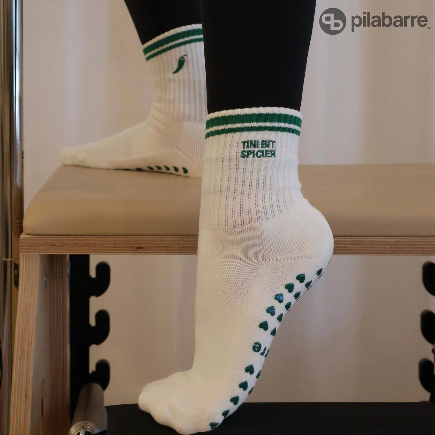 White and green Pilates grip socks with striped ribbed cuffs, embroidered chili pepper detail and green non-slip grips on the soles.