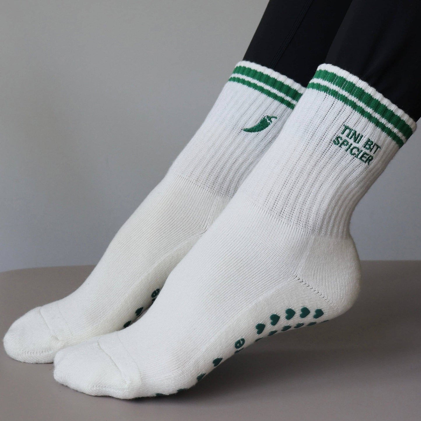 White and green Pilates grip socks with striped ribbed cuffs, embroidered chili pepper detail and green non-slip grips on the soles.