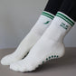 White and green Pilates grip socks with striped ribbed cuffs, embroidered chili pepper detail and green non-slip grips on the soles.