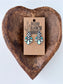 Black and white checkered western drop earrings with turquoise and iridescent stone accents displayed on a rustic wooden heart tray