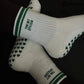 White and green Pilates grip socks with striped ribbed cuffs, embroidered chili pepper detail and green non-slip grips on the soles.