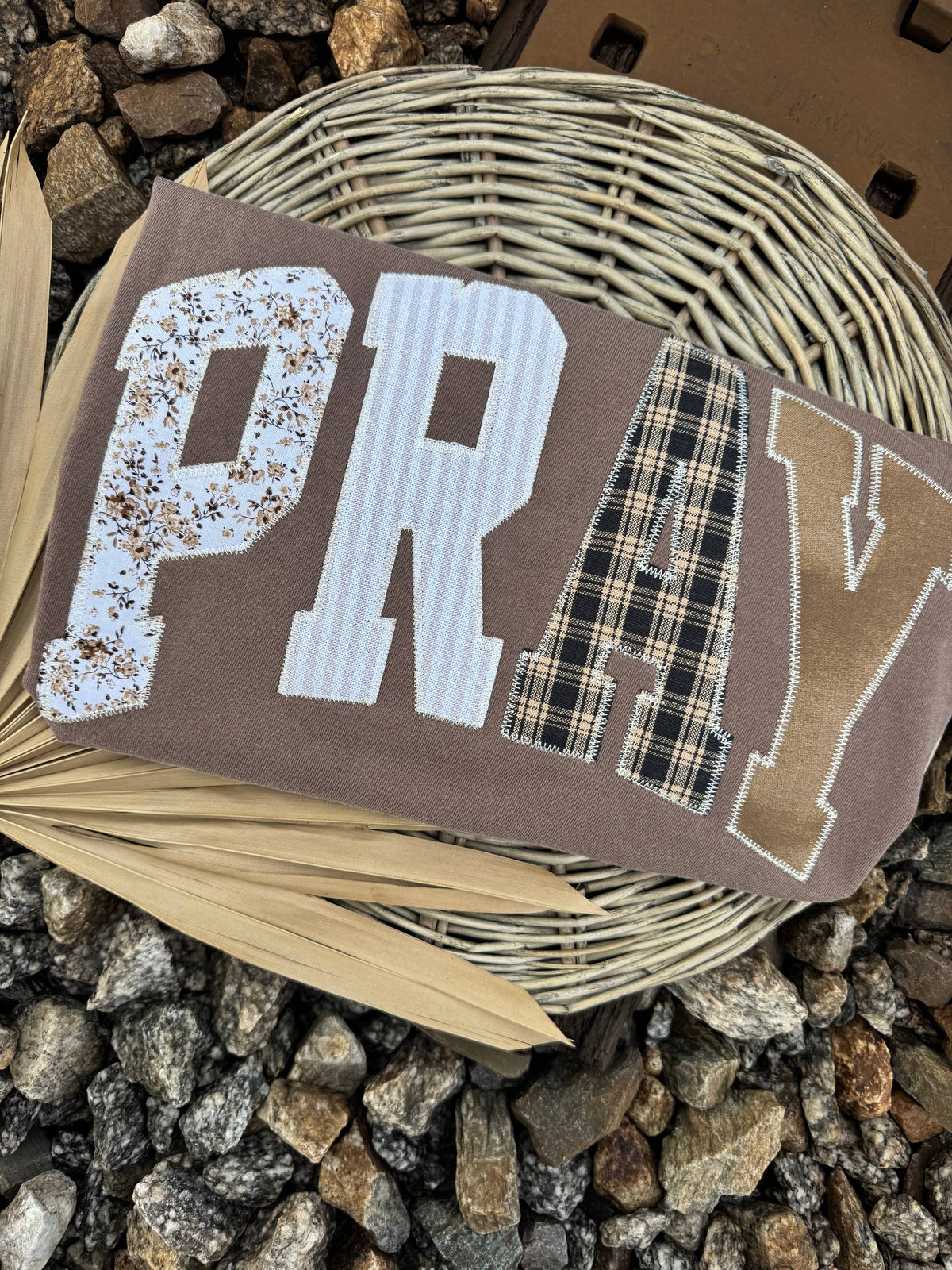 Neutral washed short sleeve PRAY graphic tee with oversized mixed-pattern patchwork lettering
