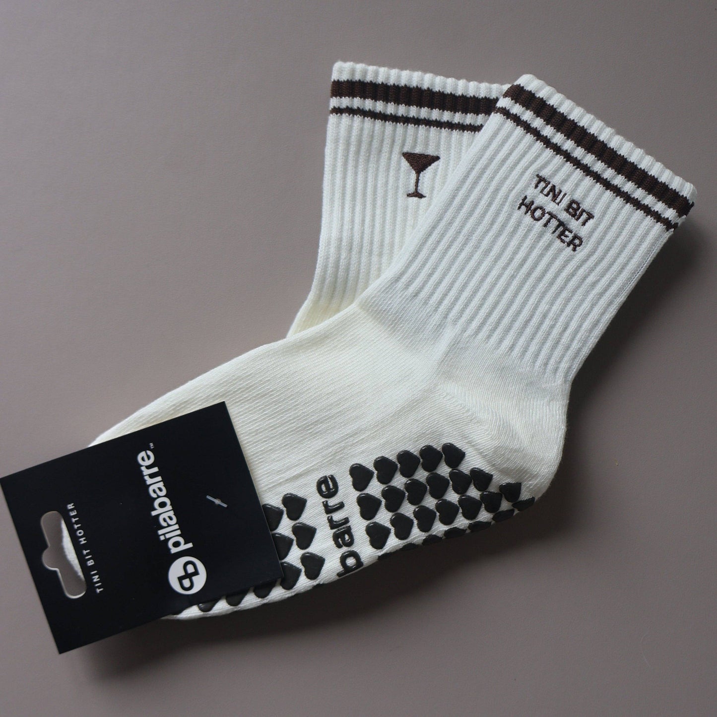 White Tiny Bit Hotter martini grip socks with contrast striped cuffs, cocktail embroidery and black heart-shaped non-slip grips.