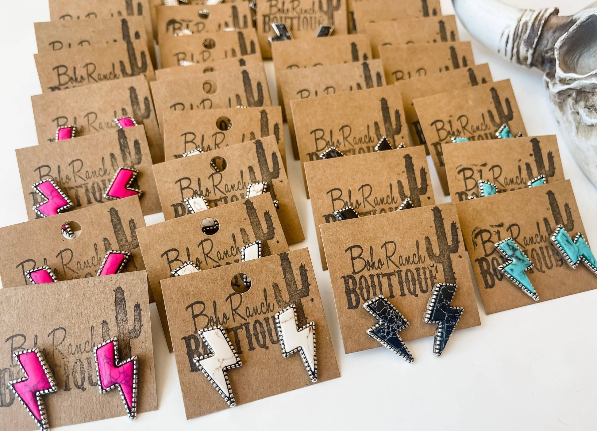 Western lightning bolt stud earrings with silver-tone detailing in pink, white and assorted colors displayed on boutique jewelry cards