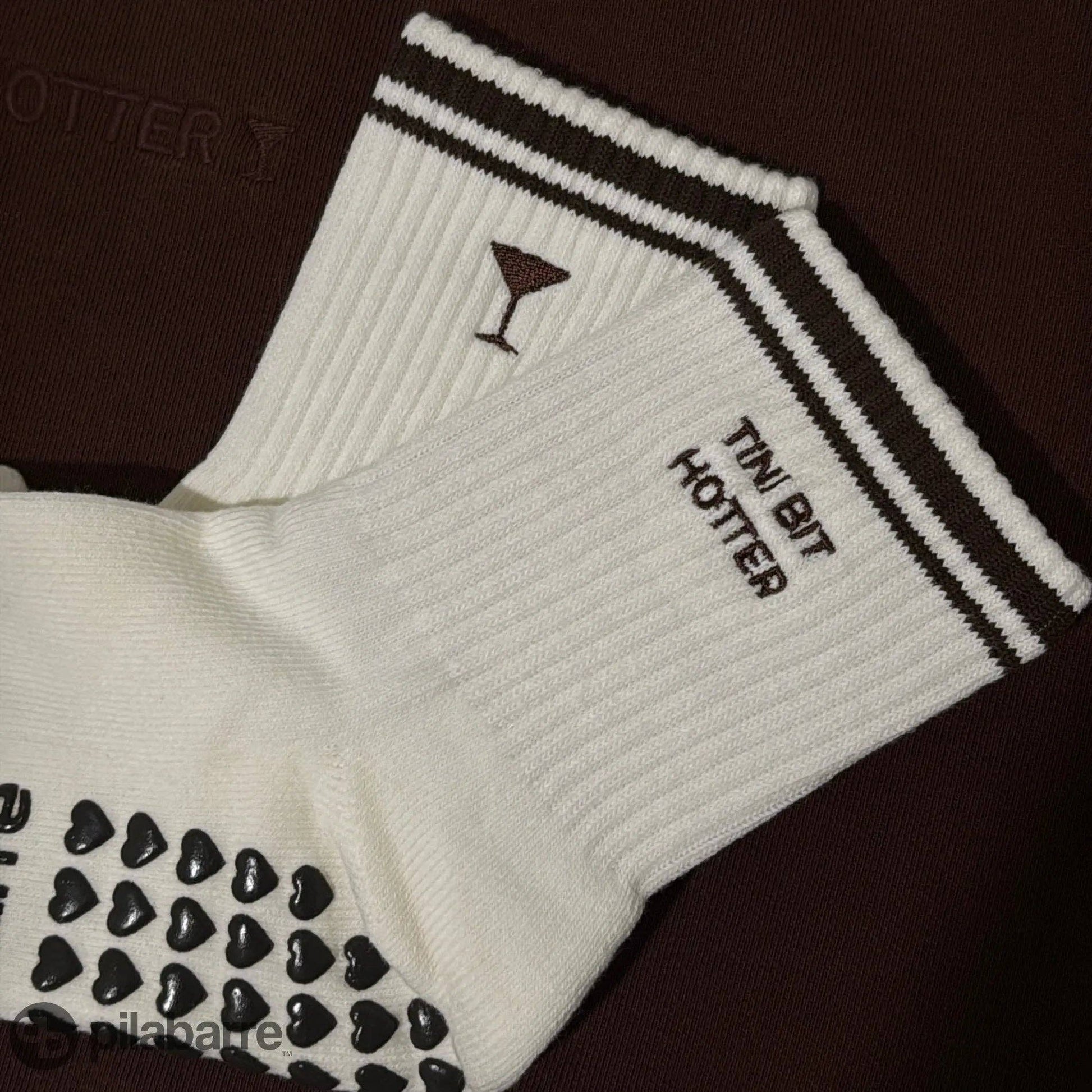 White Tiny Bit Hotter martini grip socks with contrast striped cuffs, cocktail embroidery and black heart-shaped non-slip grips.