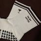 White Tiny Bit Hotter martini grip socks with contrast striped cuffs, cocktail embroidery and black heart-shaped non-slip grips.