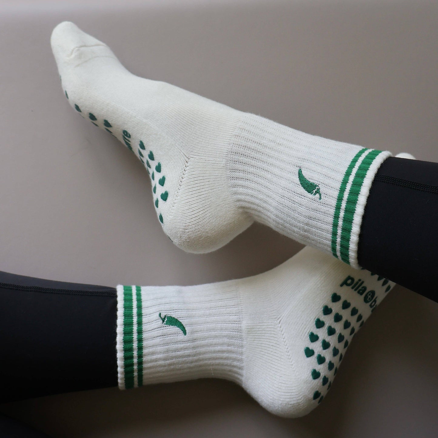 White and green Pilates grip socks with striped ribbed cuffs, embroidered chili pepper detail and green non-slip grips on the soles.