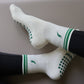 White and green Pilates grip socks with striped ribbed cuffs, embroidered chili pepper detail and green non-slip grips on the soles.