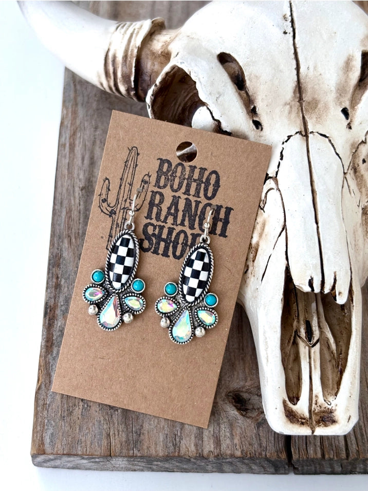 Black and white checkered western drop earrings with turquoise and iridescent stone accents displayed on a rustic wooden heart tray