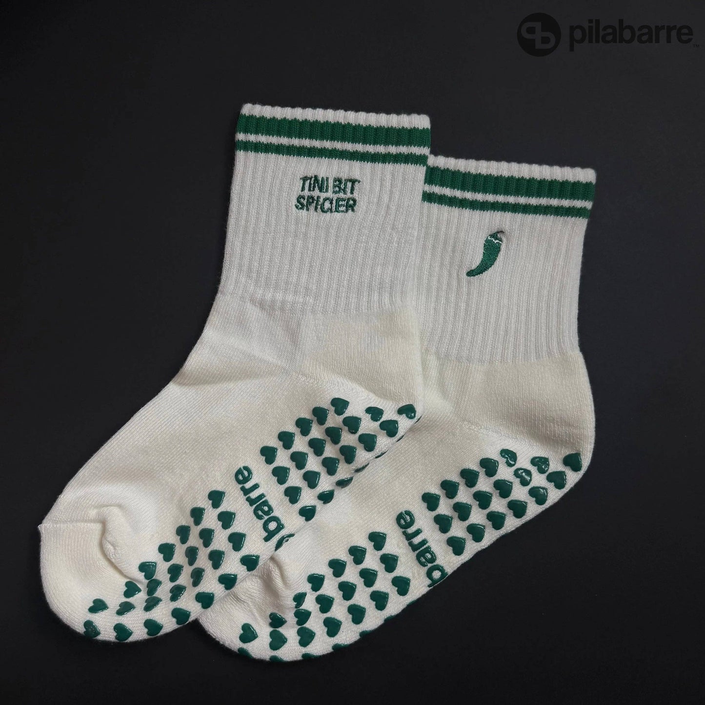 White and green Pilates grip socks with striped ribbed cuffs, embroidered chili pepper detail and green non-slip grips on the soles.