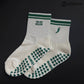 White and green Pilates grip socks with striped ribbed cuffs, embroidered chili pepper detail and green non-slip grips on the soles.