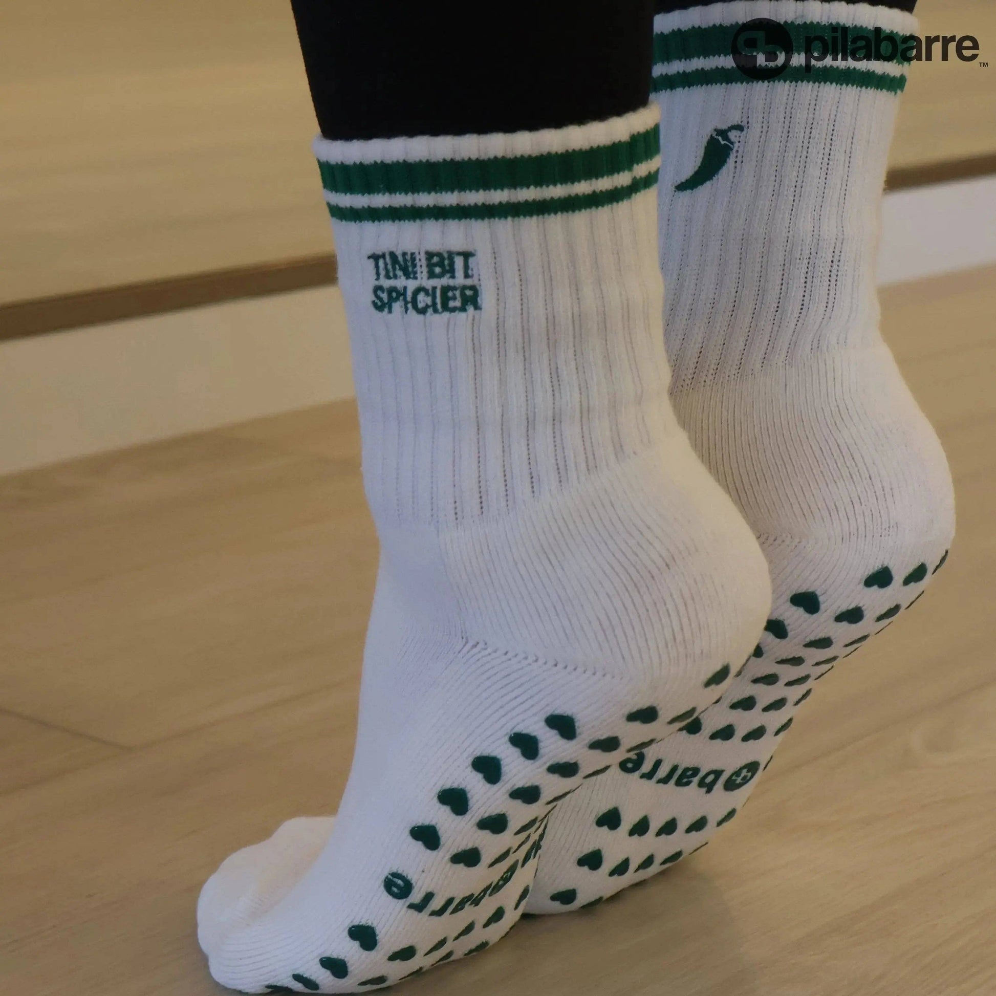 White and green Pilates grip socks with striped ribbed cuffs, embroidered chili pepper detail and green non-slip grips on the soles.