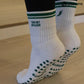White and green Pilates grip socks with striped ribbed cuffs, embroidered chili pepper detail and green non-slip grips on the soles.