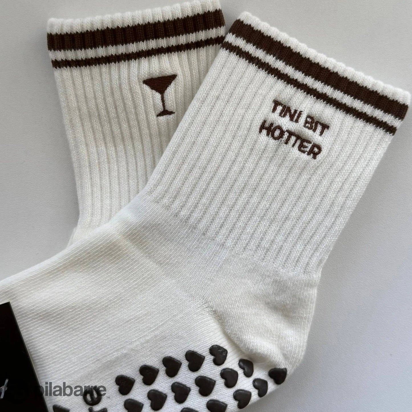 White Tiny Bit Hotter martini grip socks with contrast striped cuffs, cocktail embroidery and black heart-shaped non-slip grips.