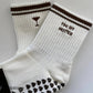 White Tiny Bit Hotter martini grip socks with contrast striped cuffs, cocktail embroidery and black heart-shaped non-slip grips.